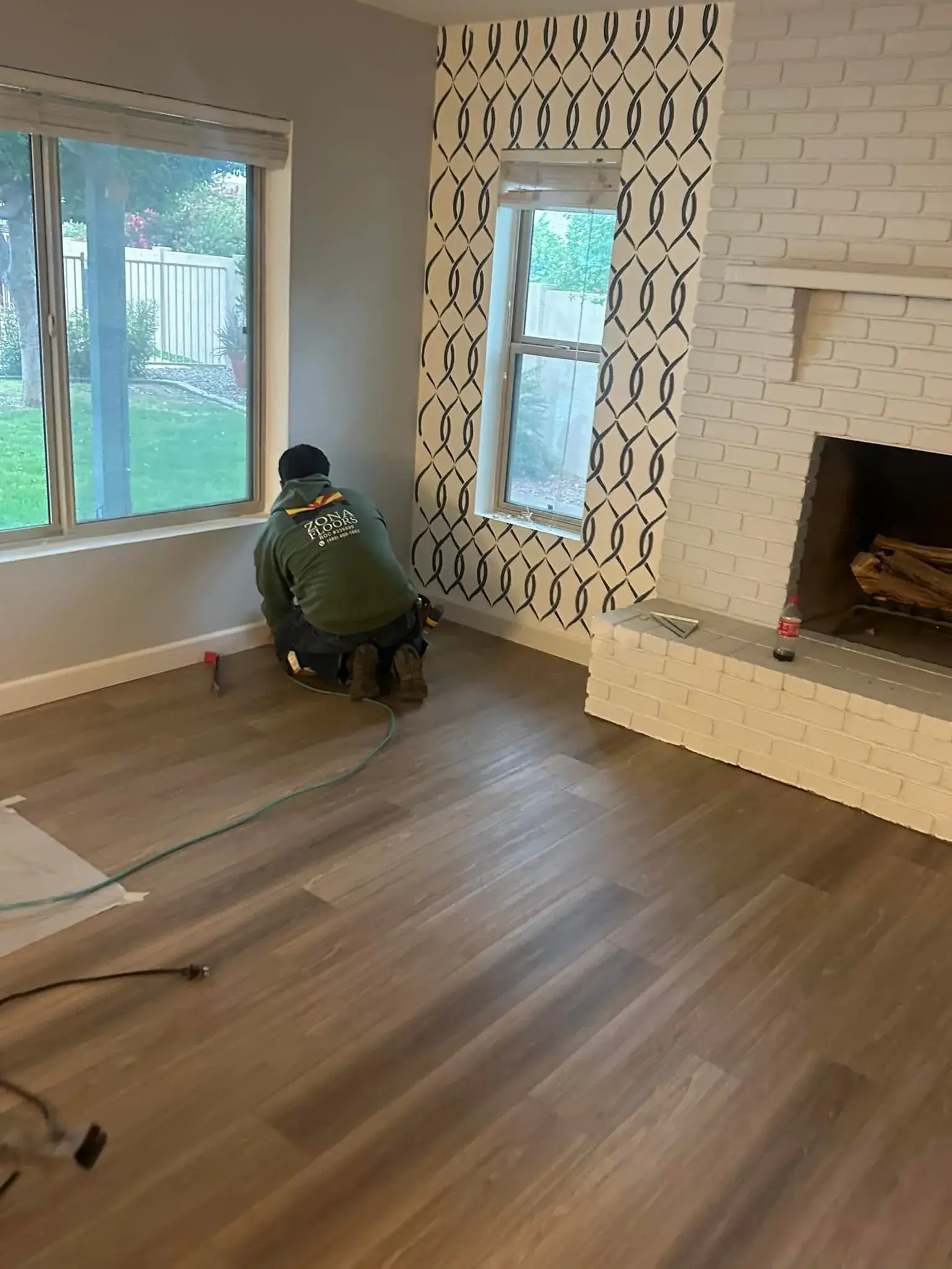 Zona Floors installer in branded shirt actively laying light oak wood-look planks at the open front door of an Arizona home