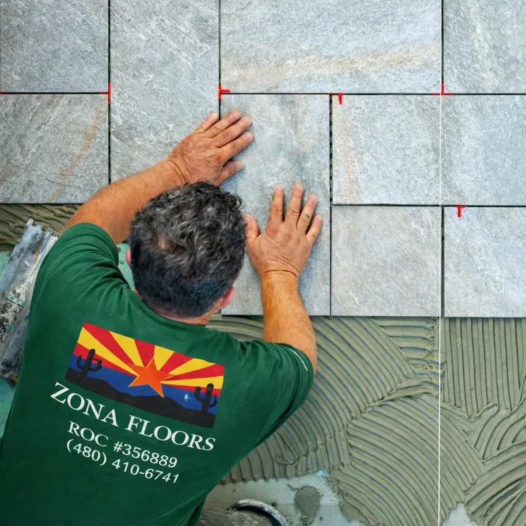 A licensed Zona Floors installer (ROC #356889) hands-on placing large-format stone tile with leveling spacers in an Arizona home